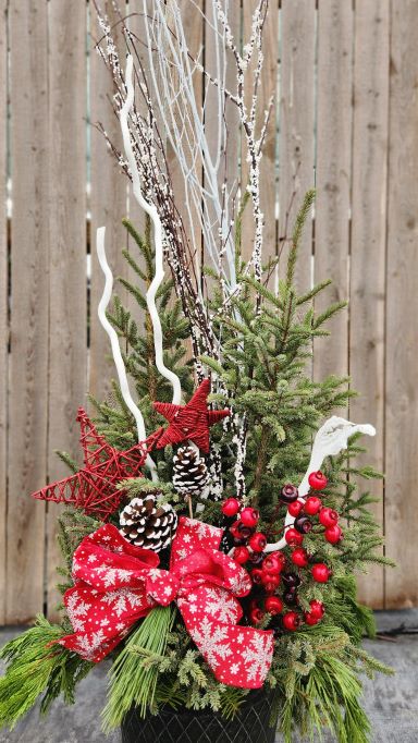 Red bow with snowflakes on spruce top pot with red stars, frosted pine cones, white twigs, and snow covered twigs