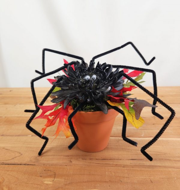 a black spider crafted from a mum, fall leaves, and ceramic pot