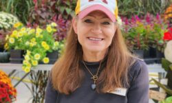 geri vogel sitting in front of fall annuals in the greenhouse wearing a Minnesota hat.