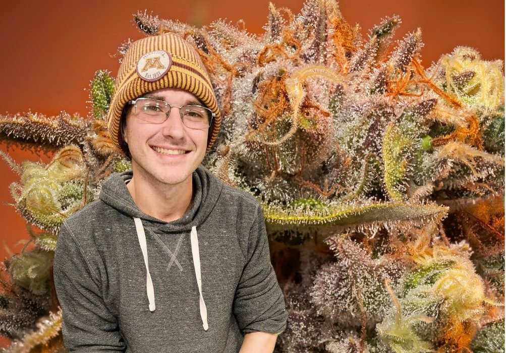 person standing in front of large picture of a cannabis plant flower